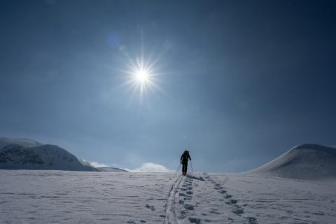 Skitourengänger aufwärts gegen Gipfel mit Sonnenstern.